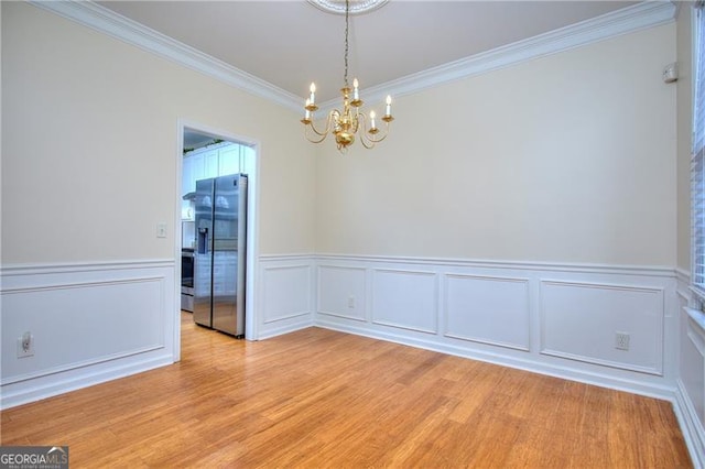 unfurnished room with a notable chandelier, ornamental molding, and light wood-type flooring