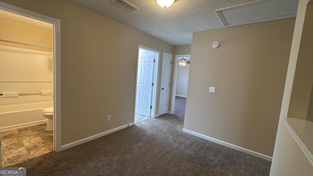 unfurnished bedroom with ensuite bath, dark carpet, and a textured ceiling