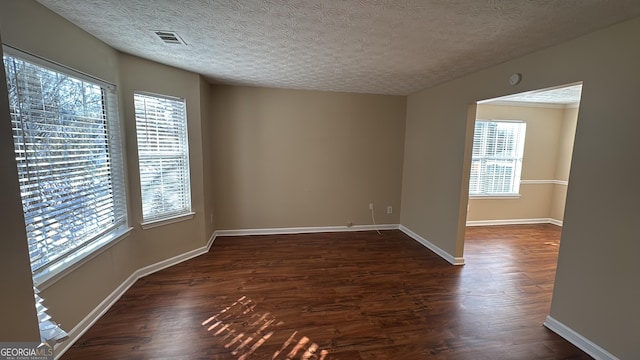 unfurnished room with a textured ceiling, a healthy amount of sunlight, and dark hardwood / wood-style floors