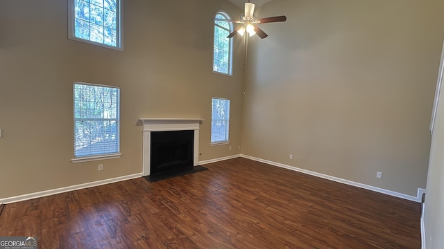 unfurnished living room featuring ceiling fan, dark wood-type flooring, and a high ceiling