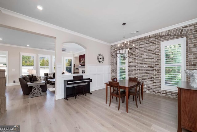 dining space featuring an inviting chandelier, brick wall, ornamental molding, and light hardwood / wood-style flooring