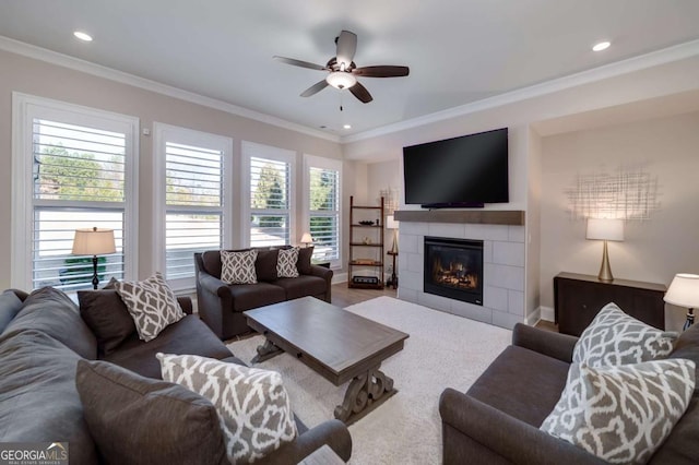 living room with ceiling fan, hardwood / wood-style floors, crown molding, and a tiled fireplace