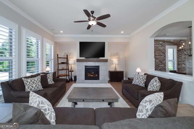 living room featuring light hardwood / wood-style flooring, crown molding, ceiling fan with notable chandelier, and a tiled fireplace