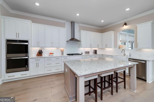 kitchen with white cabinetry, a breakfast bar area, appliances with stainless steel finishes, wall chimney range hood, and a center island