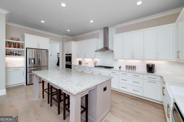 kitchen with appliances with stainless steel finishes, wall chimney range hood, white cabinetry, and a kitchen island