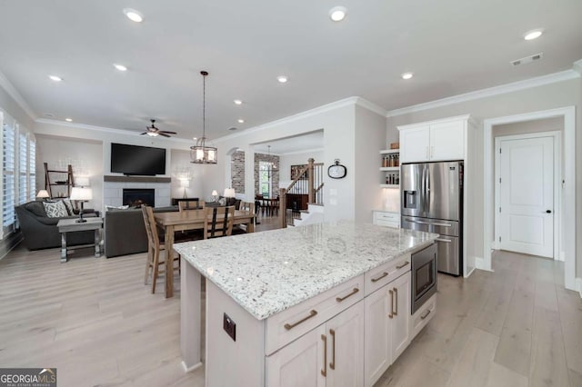 kitchen featuring stainless steel appliances, decorative light fixtures, white cabinets, a kitchen island, and light stone counters