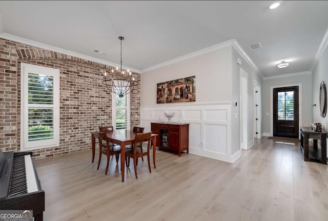 dining space with brick wall, light hardwood / wood-style flooring, a wealth of natural light, and an inviting chandelier