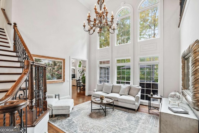 living room featuring crown molding, wood-type flooring, an inviting chandelier, and a high ceiling