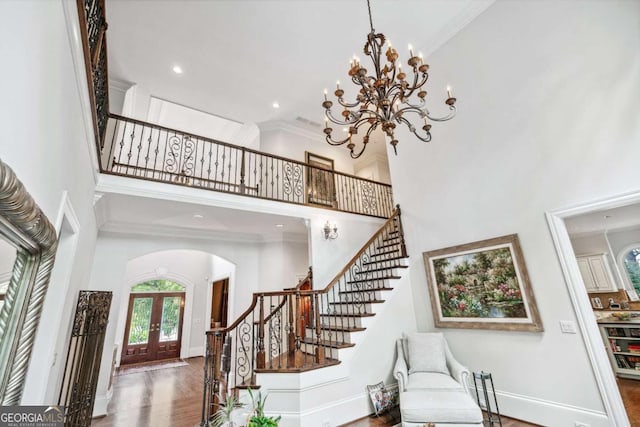 entryway featuring a towering ceiling, crown molding, french doors, dark hardwood / wood-style flooring, and a chandelier