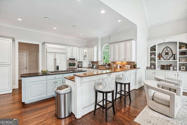 kitchen with kitchen peninsula, dark wood-type flooring, appliances with stainless steel finishes, ornamental molding, and white cabinets