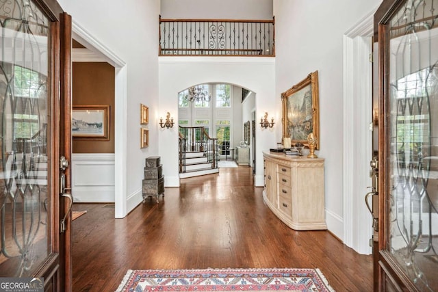 foyer with dark wood-type flooring, crown molding, and a towering ceiling