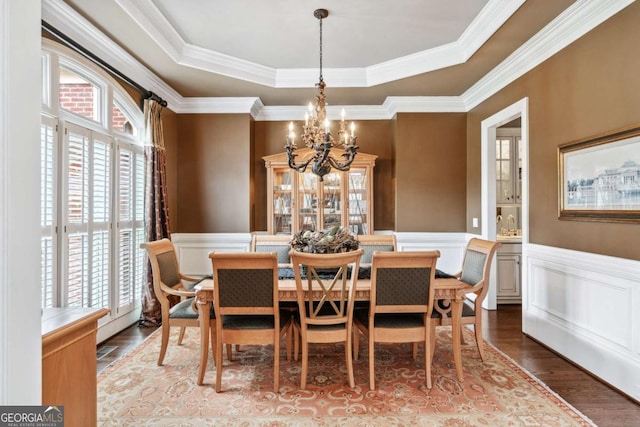 dining area featuring a raised ceiling, ornamental molding, a chandelier, and hardwood / wood-style flooring