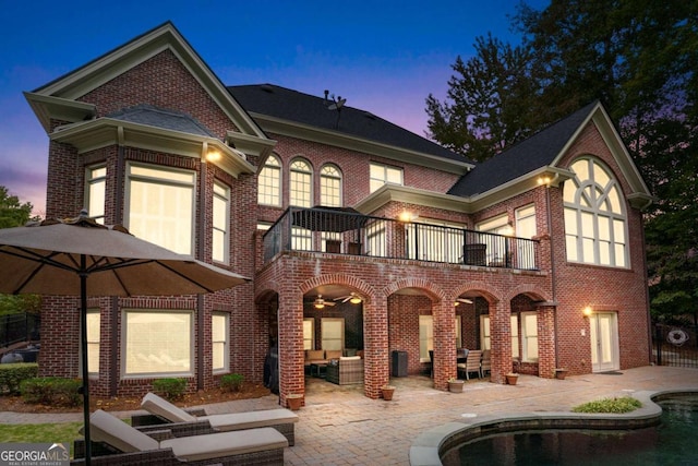 back house at dusk featuring a patio area, outdoor lounge area, and a balcony