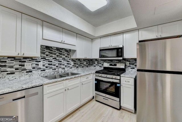 kitchen with white cabinetry, stainless steel appliances, backsplash, light stone countertops, and sink