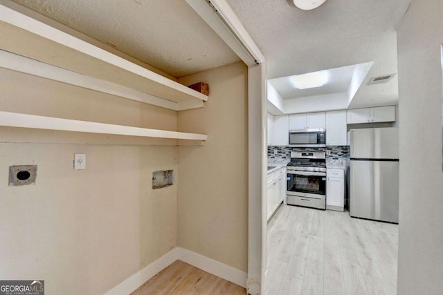 kitchen featuring light hardwood / wood-style floors, appliances with stainless steel finishes, a raised ceiling, tasteful backsplash, and white cabinets