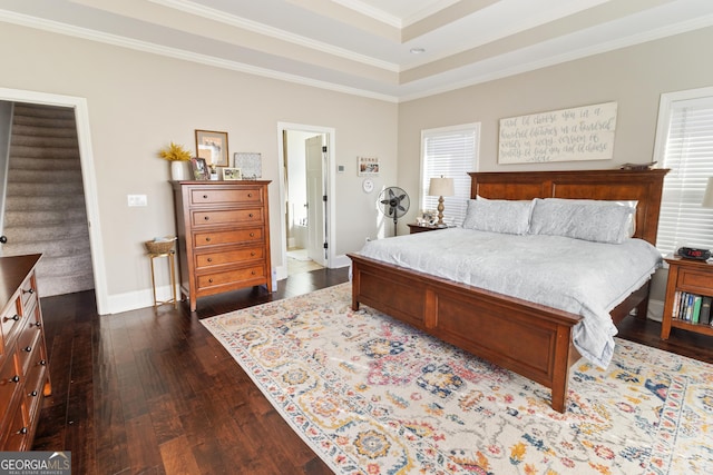 bedroom with dark wood-type flooring, crown molding, connected bathroom, and a tray ceiling