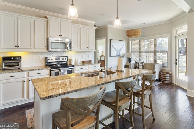 kitchen with pendant lighting, sink, appliances with stainless steel finishes, an island with sink, and light stone counters