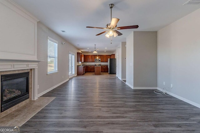 unfurnished living room featuring ceiling fan, dark hardwood / wood-style floors, and a tiled fireplace