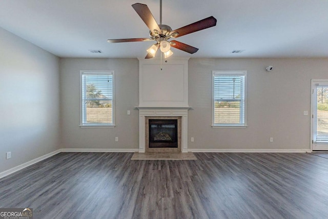 unfurnished living room featuring ceiling fan, a high end fireplace, a healthy amount of sunlight, and dark hardwood / wood-style flooring