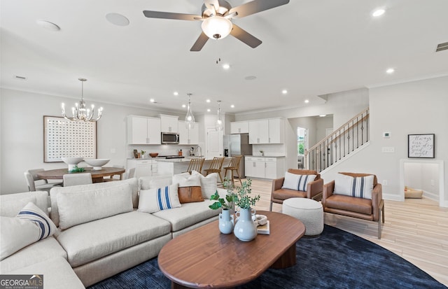 living room featuring ceiling fan with notable chandelier, ornamental molding, and light hardwood / wood-style floors