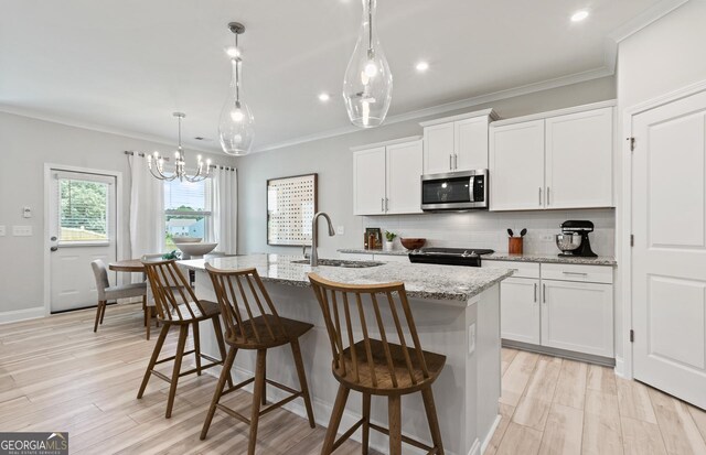 kitchen with an island with sink, electric range oven, pendant lighting, white cabinets, and light stone counters