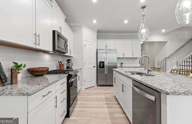 kitchen with stainless steel appliances, pendant lighting, white cabinets, and a kitchen island with sink