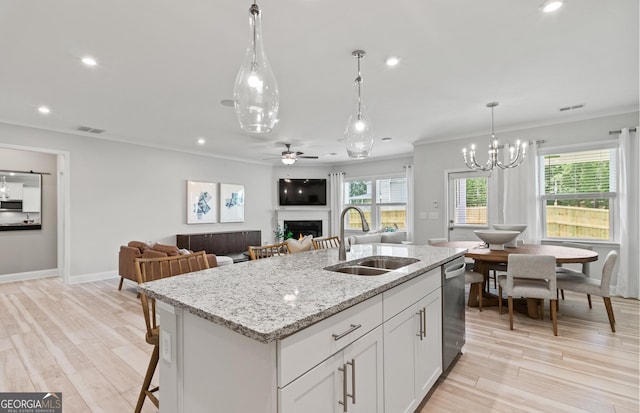 kitchen featuring white cabinets, a kitchen island with sink, sink, and light stone counters