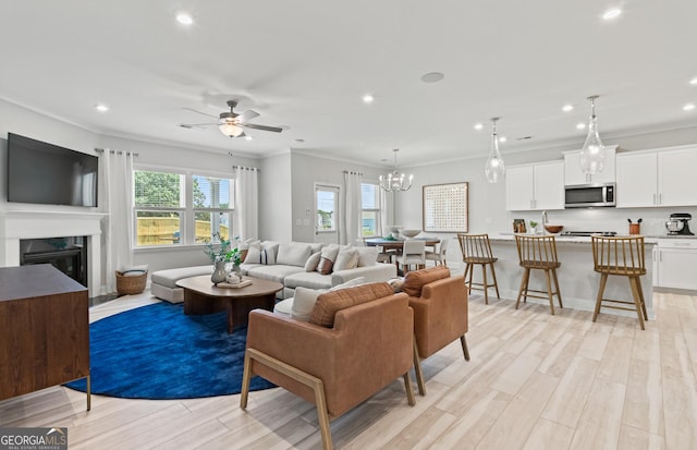 living room with a premium fireplace, ornamental molding, ceiling fan with notable chandelier, and light hardwood / wood-style flooring