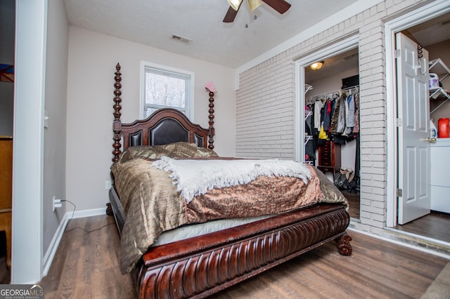 bedroom with a walk in closet, brick wall, a closet, a textured ceiling, and dark wood-type flooring