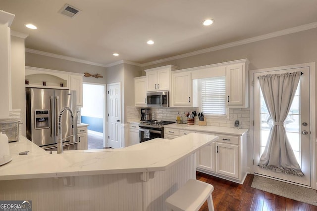 kitchen featuring tasteful backsplash, white cabinetry, dark wood-type flooring, appliances with stainless steel finishes, and a kitchen breakfast bar