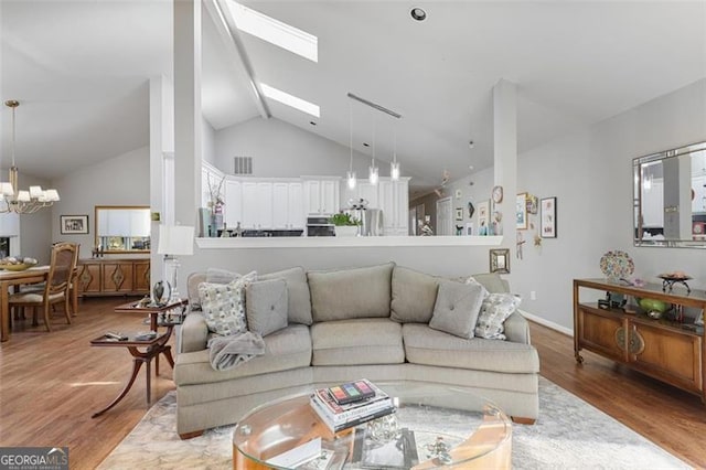 living room with an inviting chandelier, a skylight, light hardwood / wood-style flooring, and high vaulted ceiling