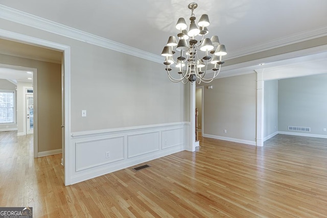 spare room featuring light hardwood / wood-style floors, decorative columns, a chandelier, and ornamental molding