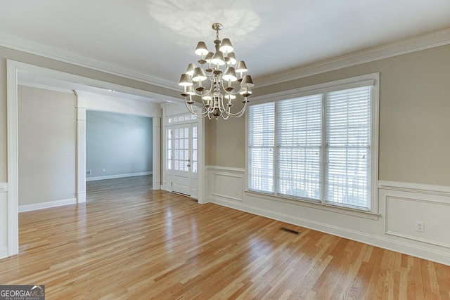 unfurnished dining area featuring light wood-type flooring, crown molding, and a notable chandelier