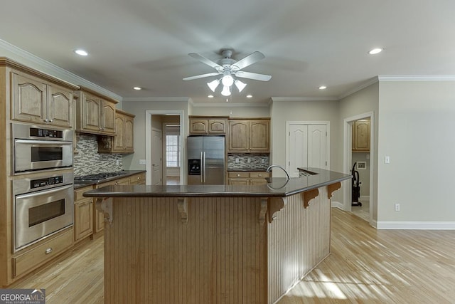 kitchen with a breakfast bar area, stainless steel appliances, backsplash, a kitchen island with sink, and ornamental molding