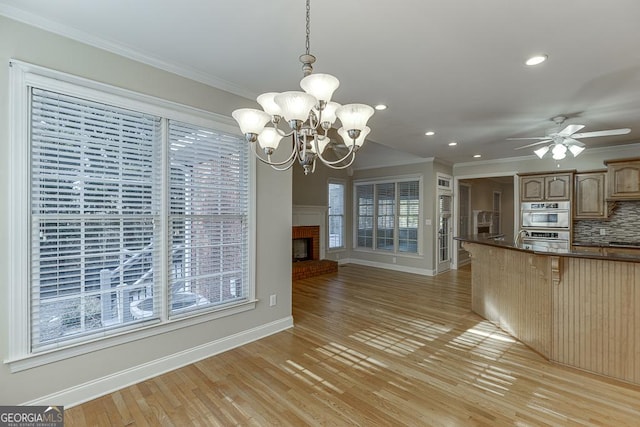 kitchen featuring ceiling fan with notable chandelier, a fireplace, decorative backsplash, hanging light fixtures, and light wood-type flooring