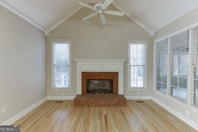 unfurnished living room featuring a brick fireplace, crown molding, lofted ceiling, and a healthy amount of sunlight