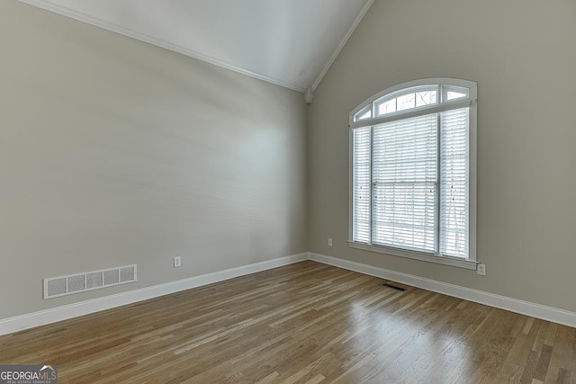 empty room featuring vaulted ceiling, ornamental molding, and hardwood / wood-style flooring