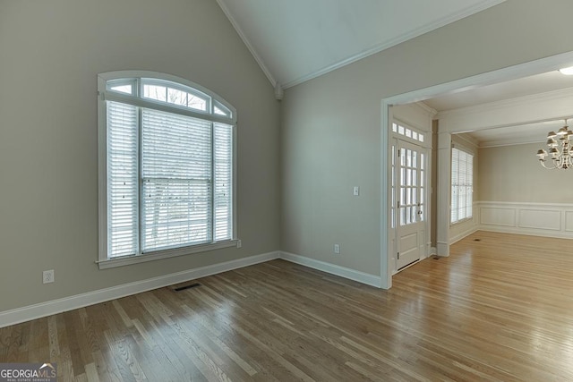 empty room with lofted ceiling, an inviting chandelier, ornamental molding, and hardwood / wood-style floors