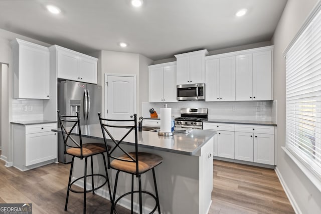 kitchen with a center island with sink, tasteful backsplash, stainless steel appliances, and white cabinetry