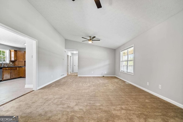 unfurnished living room with carpet, a textured ceiling, sink, vaulted ceiling, and ceiling fan