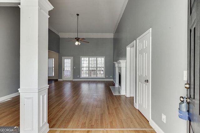 unfurnished living room featuring ceiling fan, a towering ceiling, crown molding, light hardwood / wood-style flooring, and ornate columns