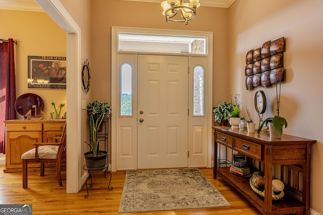 entrance foyer with an inviting chandelier, ornamental molding, and light hardwood / wood-style flooring