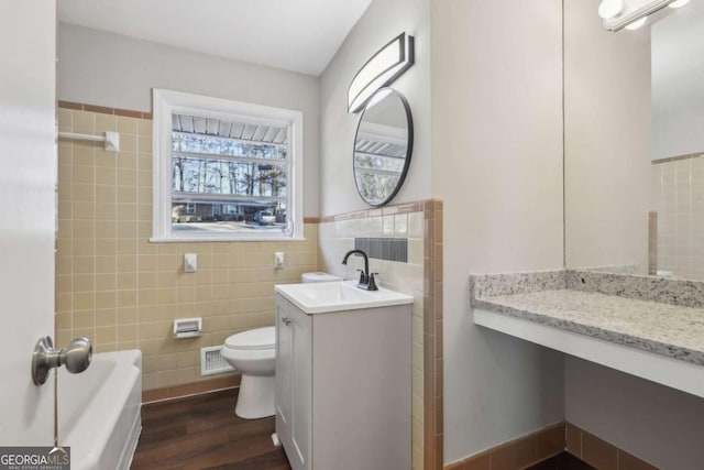 bathroom with hardwood / wood-style floors, vanity, a tub, tile walls, and toilet