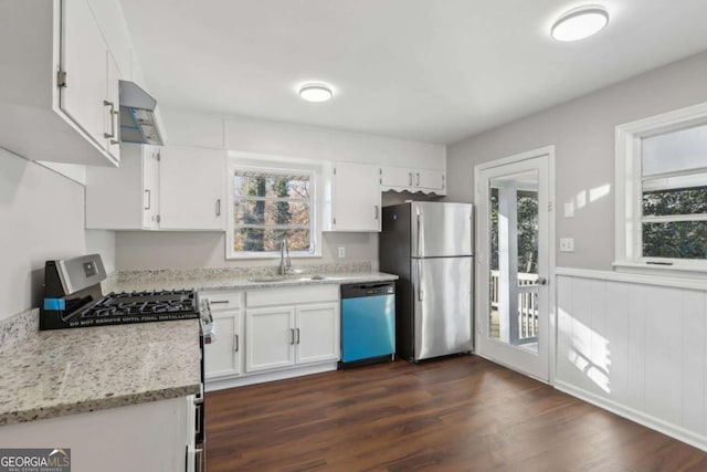 kitchen with appliances with stainless steel finishes, exhaust hood, white cabinetry, sink, and light stone counters