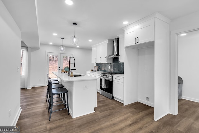 kitchen with stainless steel range with gas cooktop, an island with sink, sink, white cabinets, and wall chimney exhaust hood