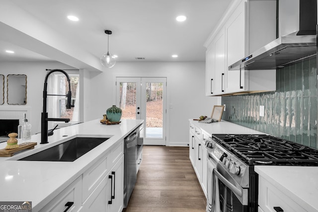 kitchen with appliances with stainless steel finishes, pendant lighting, sink, white cabinets, and wall chimney range hood