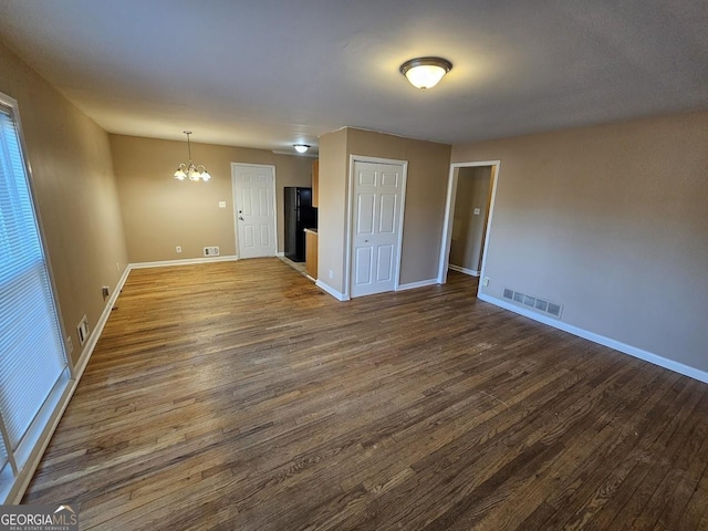 spare room featuring dark wood-type flooring and a chandelier