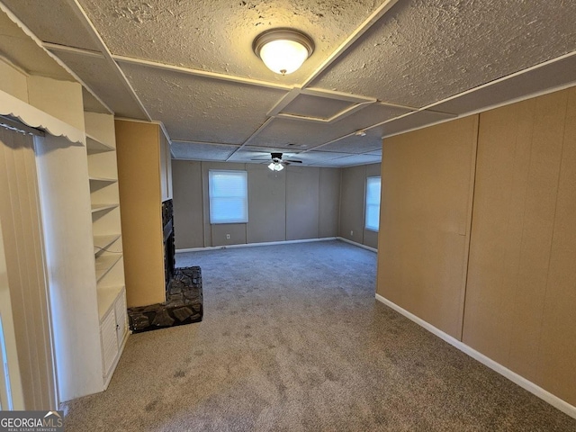 basement featuring ceiling fan, carpet flooring, a healthy amount of sunlight, and a fireplace