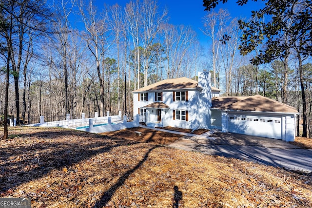 view of front facade with driveway, fence, a chimney, and an attached garage