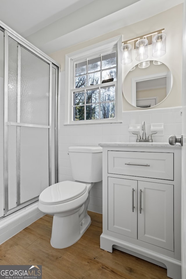 bathroom with toilet, vanity, tile walls, hardwood / wood-style floors, and a shower with door